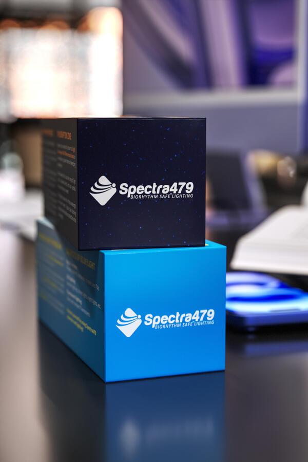 Two stacked Spectra479 eyewear boxes, one dark blue and one light blue, showing the brand logo, on a reflective office desk.