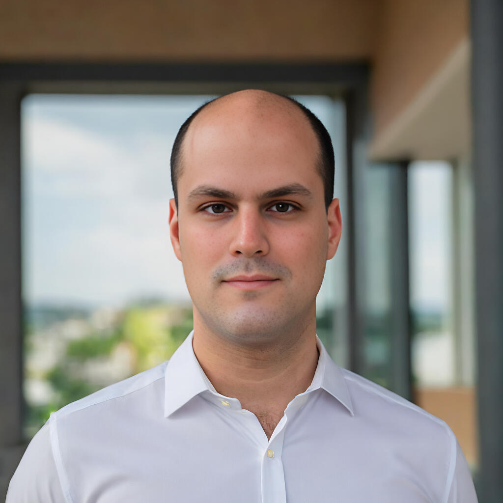 Headshot of Luís Camacho, packaging graphic designer and site owner, smiling slightly and wearing a white collared shirt, set against a blurred background with a window view.
